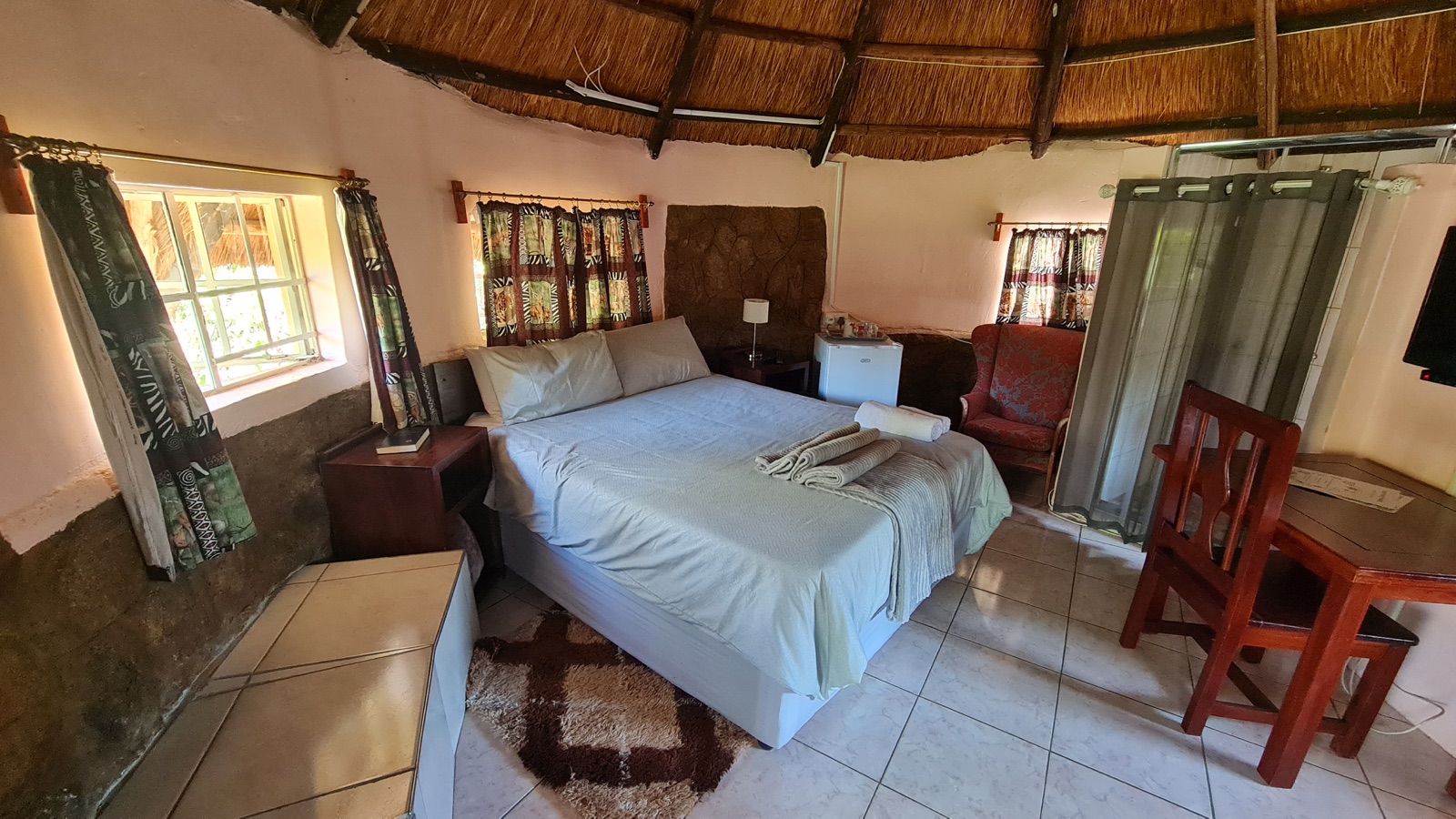 Thatched rondavel room with desk and ensuite area at Lynn's Guesthouse